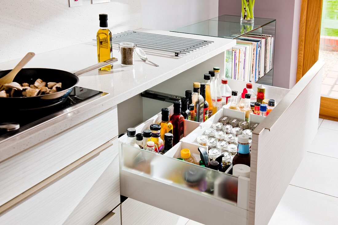 A white kitchen counter with an open drawer revealing spices and bottles