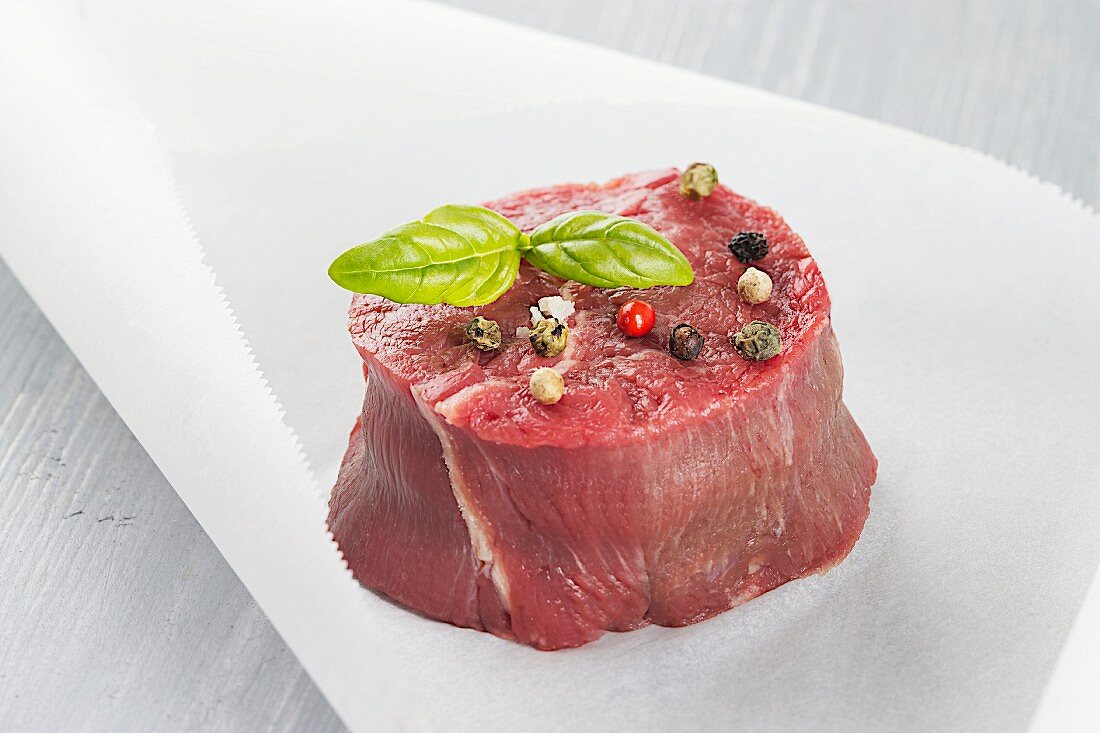 Raw beef fillet wiht peppercorns and basil leaves