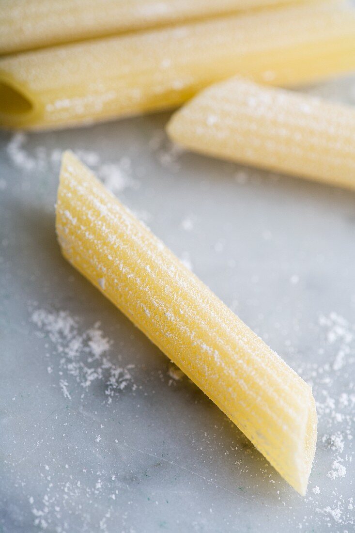 Frische Penne Rigate Nudeln auf bemehlter Marmorfläche