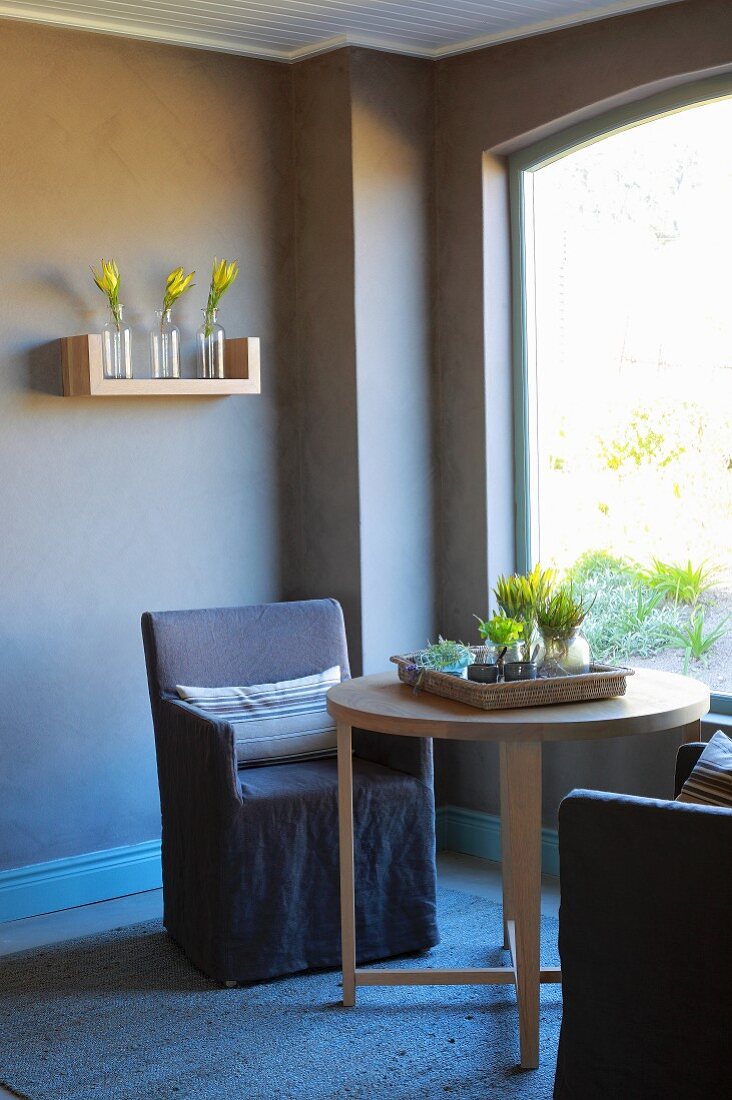 Armchair and round wooden table next to window in corner of brown-painted room