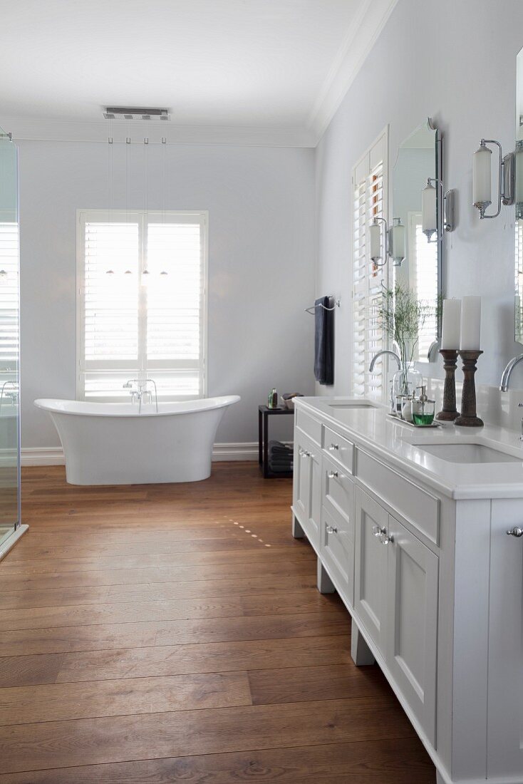 White, country-house-style washstand with twin sinks and free-standing bathtub in front of French windows