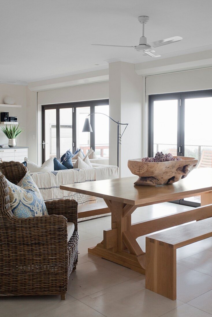 Modern bench, wooden table and wicker armchair in open-plan interior