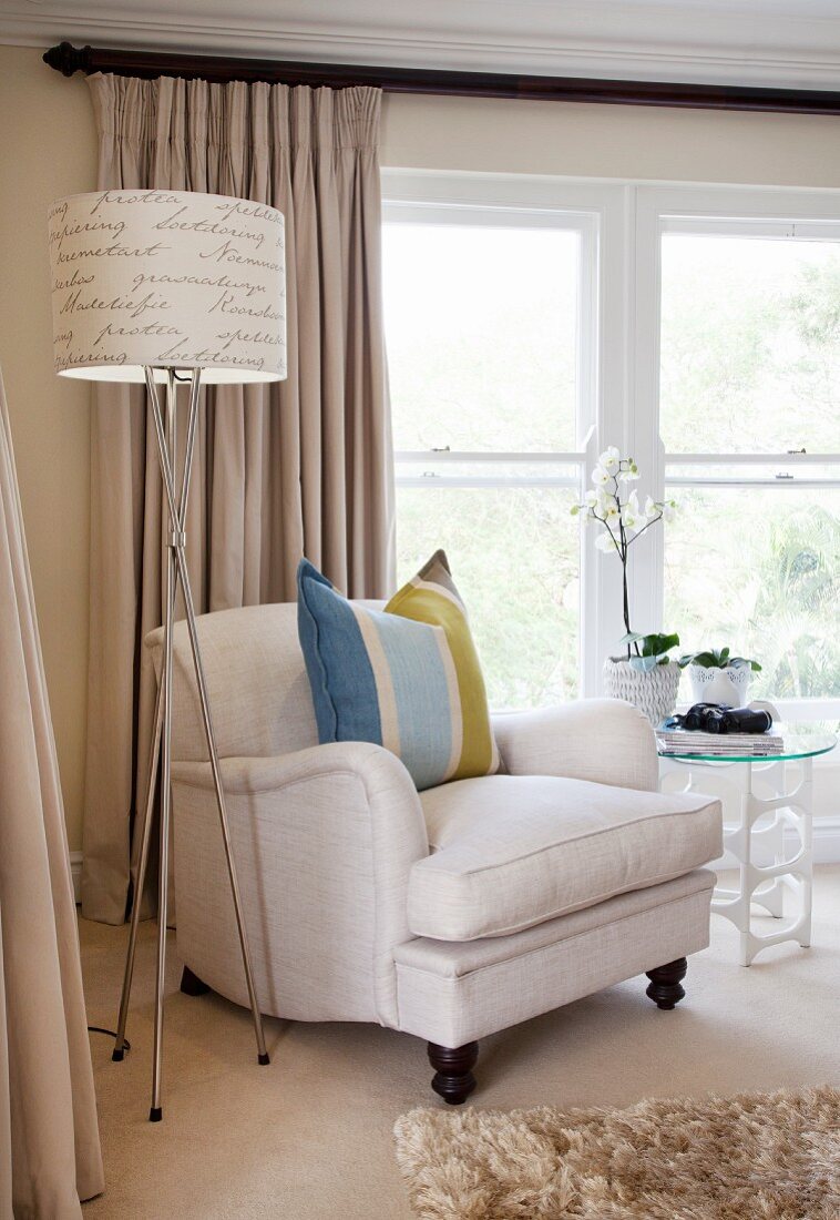 Pale armchair with striped scatter cushion next to standard lamp with lettering on lampshade