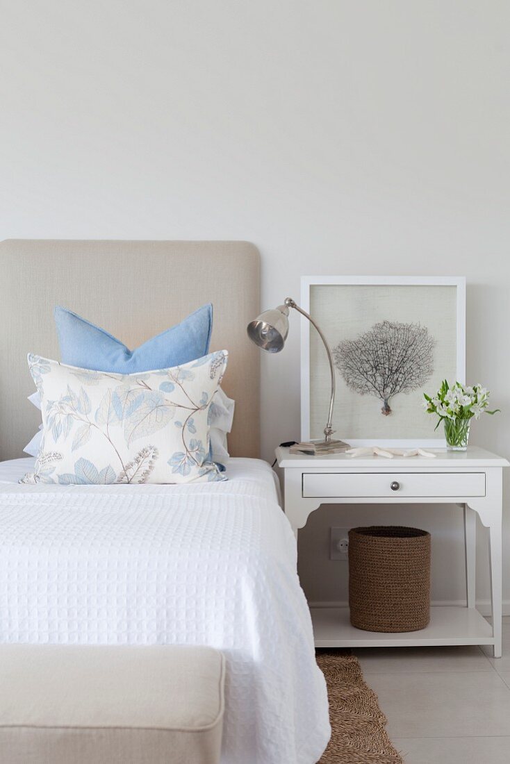 Double bed with white bedspread, arranged scatter cushions and white-painted bedside table