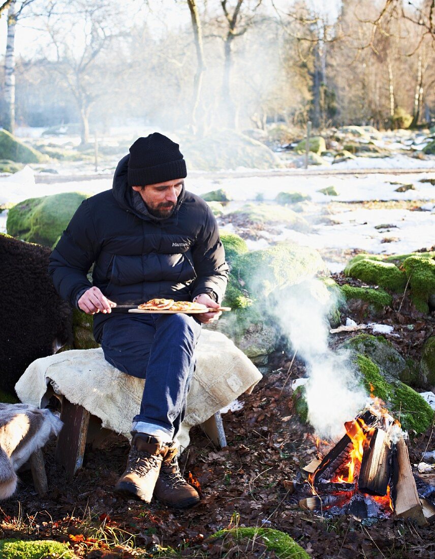 Mann isst Pizza am Lagerfeuer im Winter