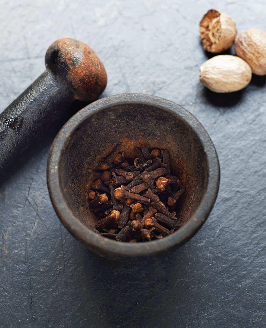 Clove in a mortar with a pester and nutmegs next to it