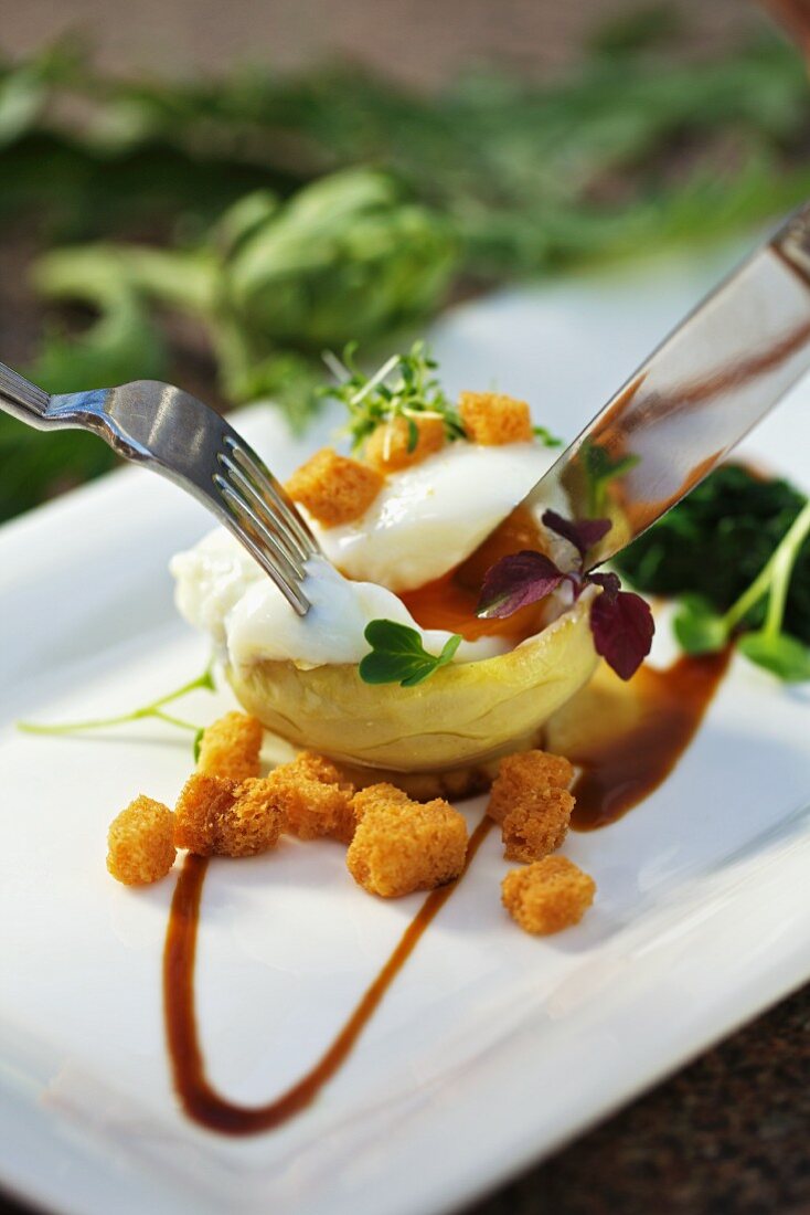 A poached egg served an artichoke heart with Madeira sauce and croutons