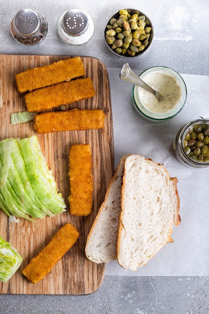 A fish finger sandwich with tartare sauce and capers being made