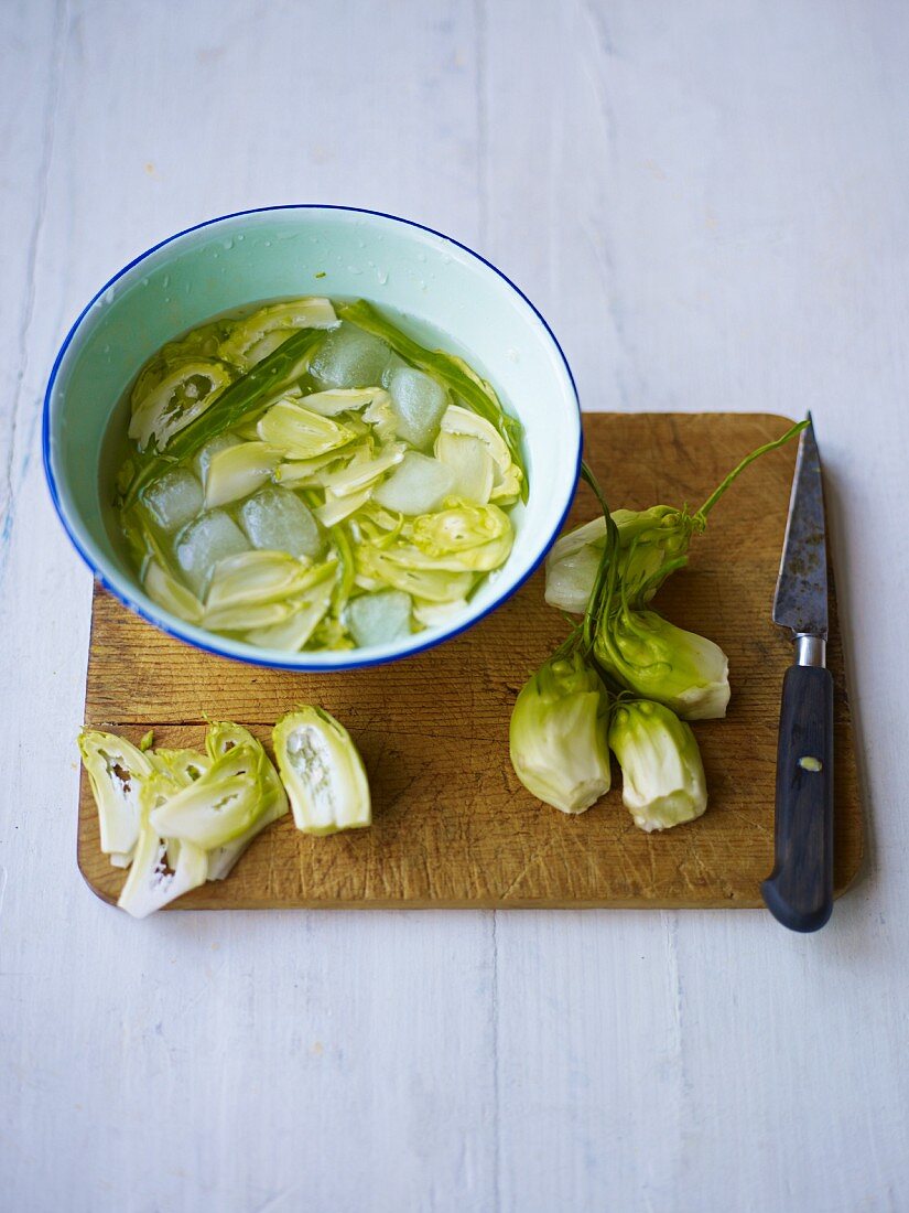 Puntarelle-Herzen (italienische Salatsorte, Zichorienart) auf Schneidebrett, geschnitten und in Schüssel mit Eiswasser