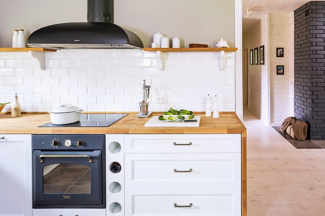 Kitchen counter with wooden worksurface and built-in cooker below extractor hood next to cabinet with white drawer fronts