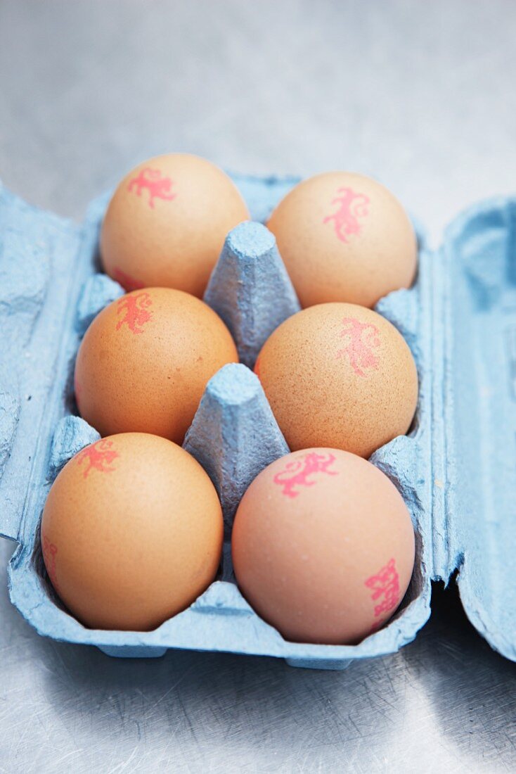 Six brown eggs with stamps in an egg box