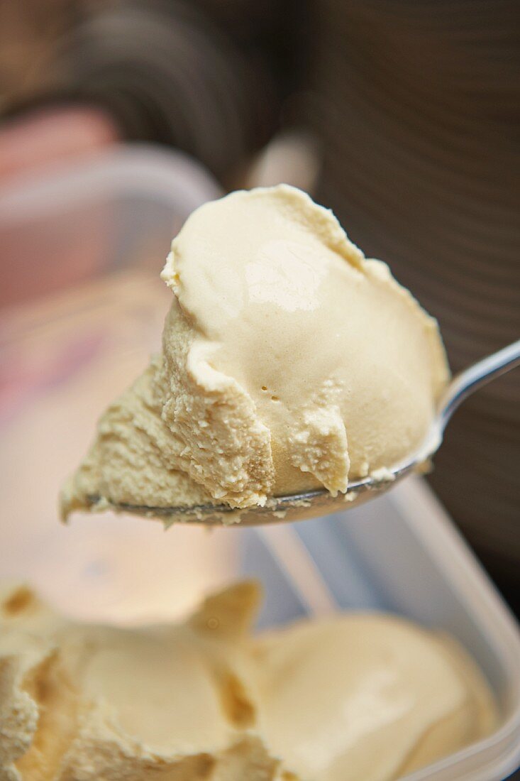 Hmemade toffee ice cream on a spoon above and ice cream container