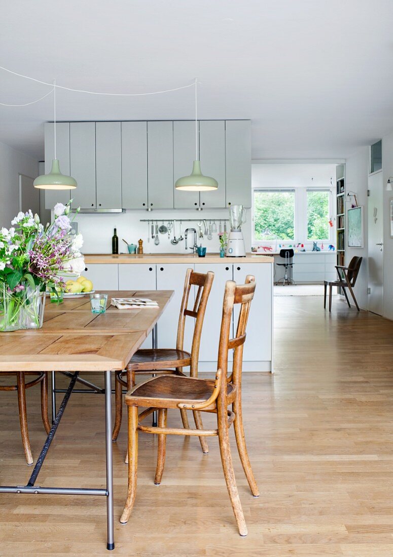 Egon Eiermann table frame with wooden top and old wooden chairs in front of open-plan kitchen in spacious interior