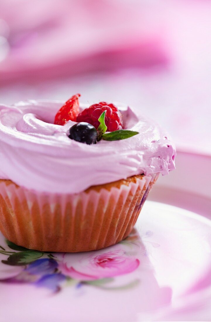A cupcake topped with strawberry cream and fresh berries