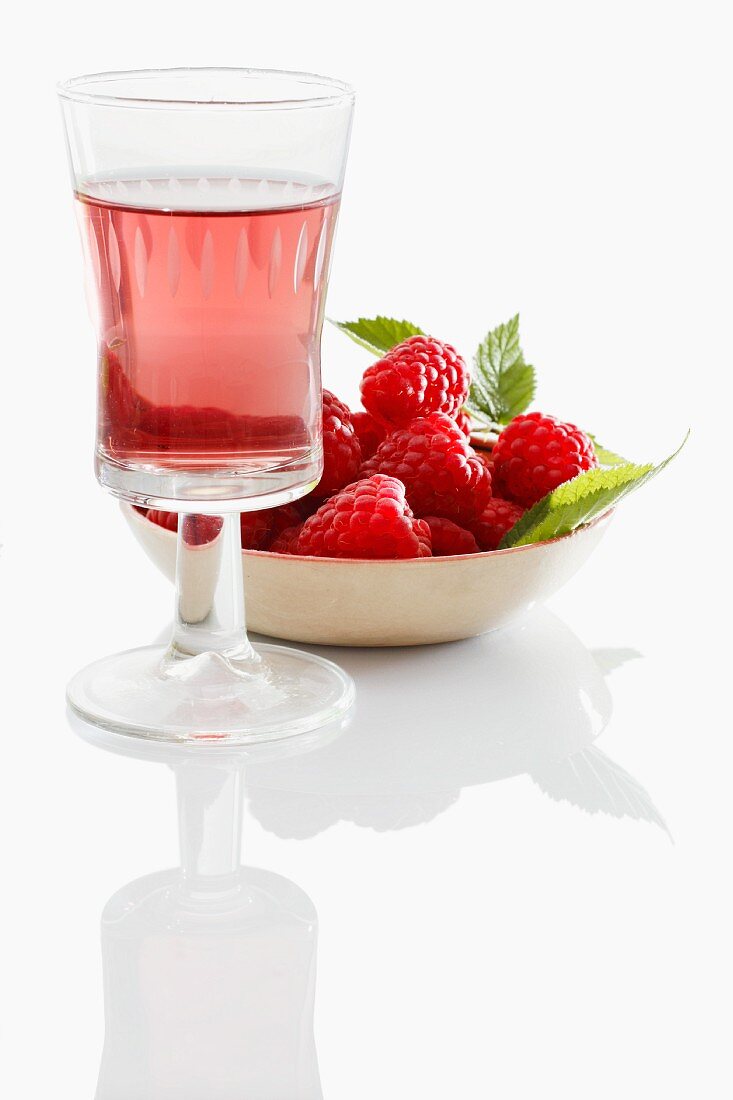 A glass of raspberry liqueur in front of a bowl of fresh raspberries