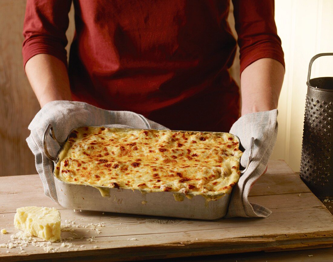 A woman holding a dish of freshly baked lasagne