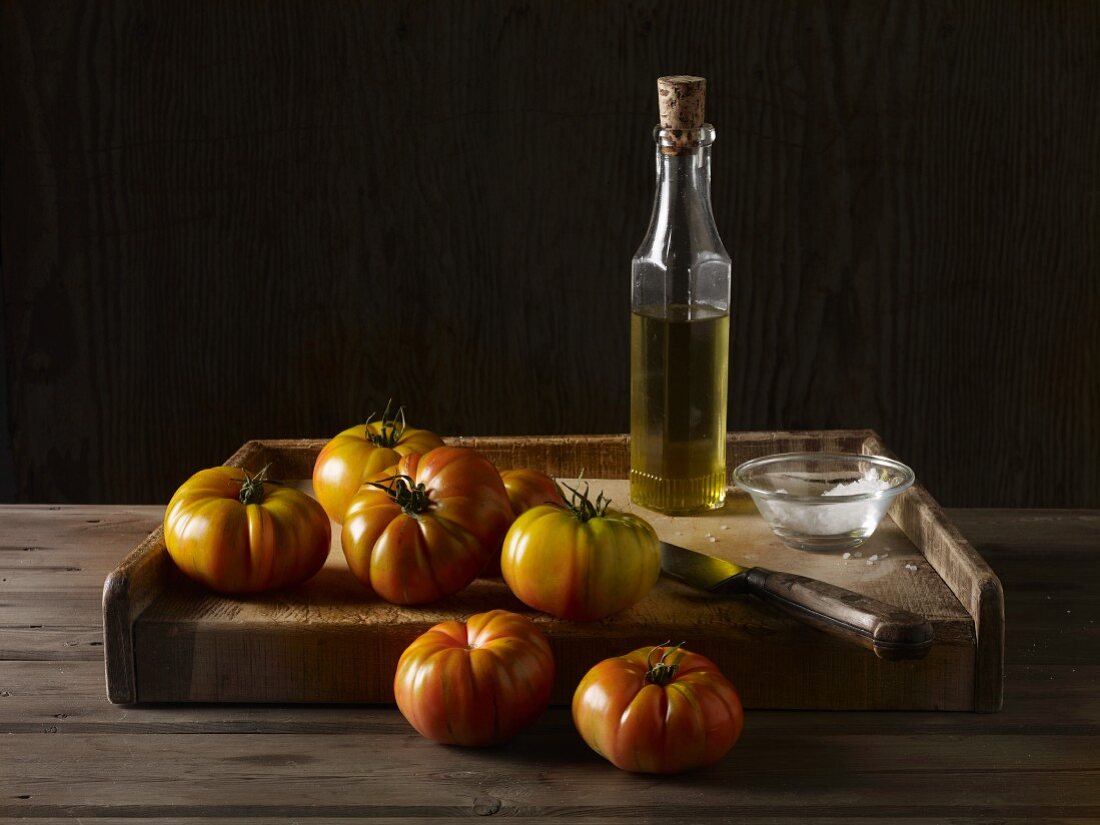 Marmande tomatoes on a wooden board with olive oil, salt and a knife