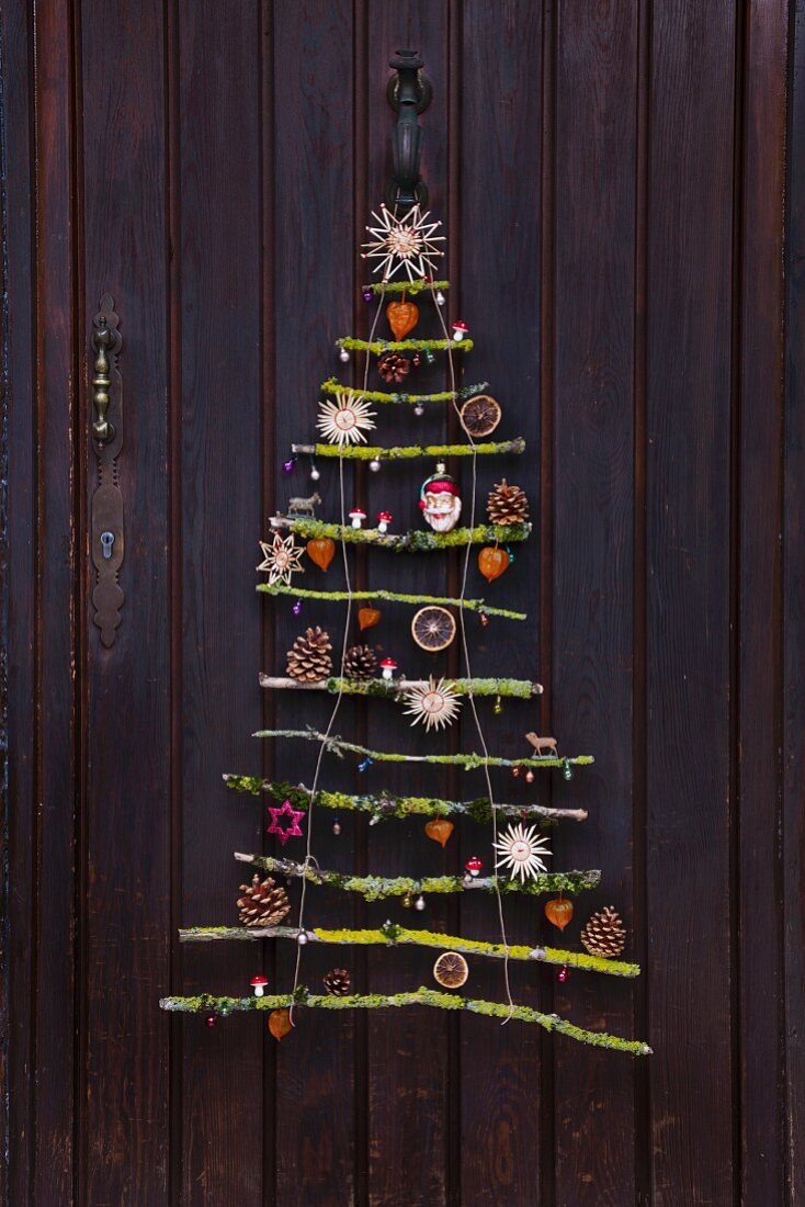 Stylised Christmas tree made from mossy branches with natural decorations and straw stars hanging on front door