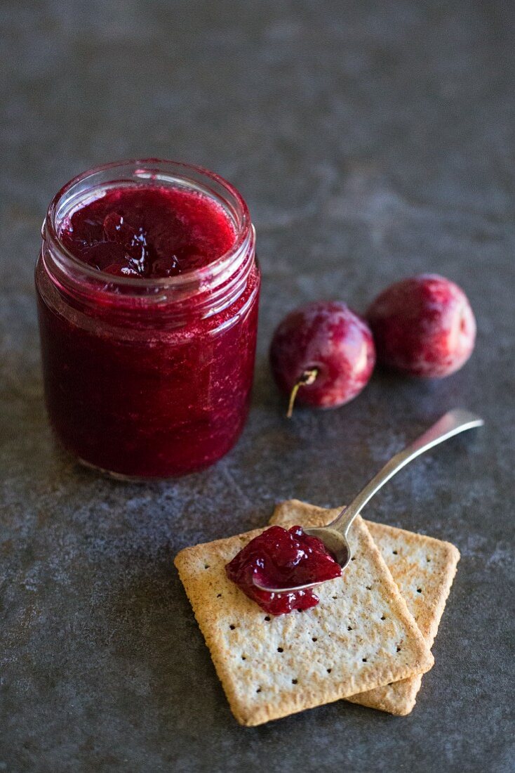 Plum jam in a jar and on a spoon with crackers