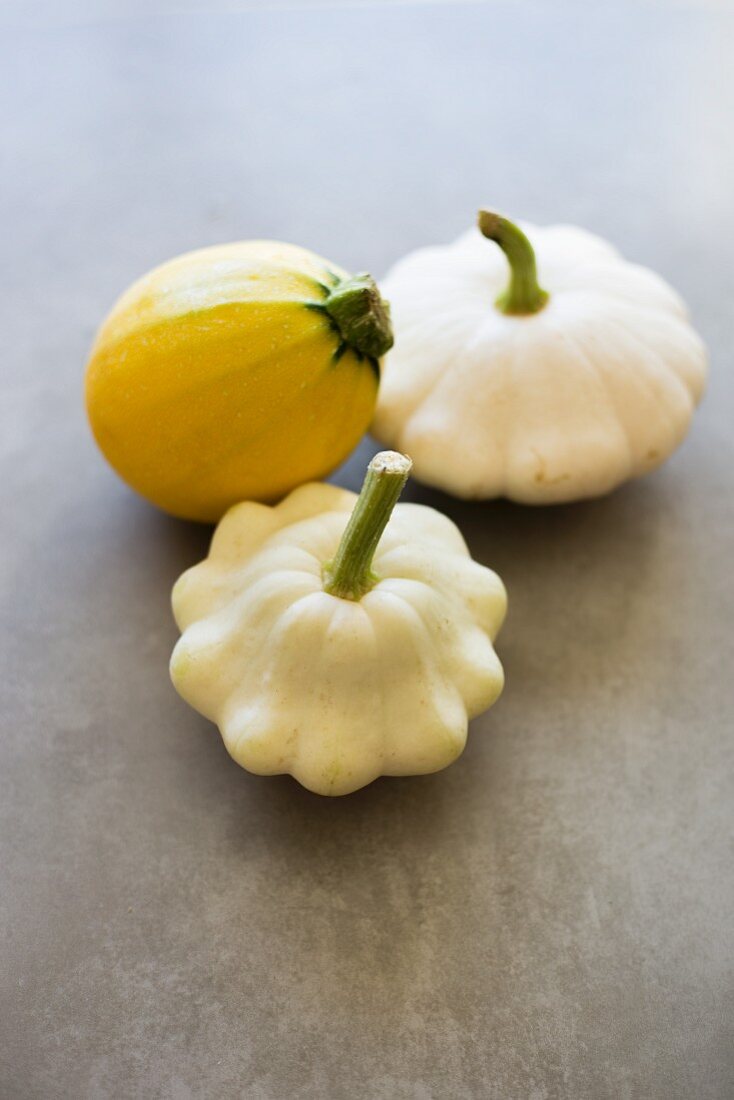 Two white patty pan squashes and a yellow summer squash on a grey surface