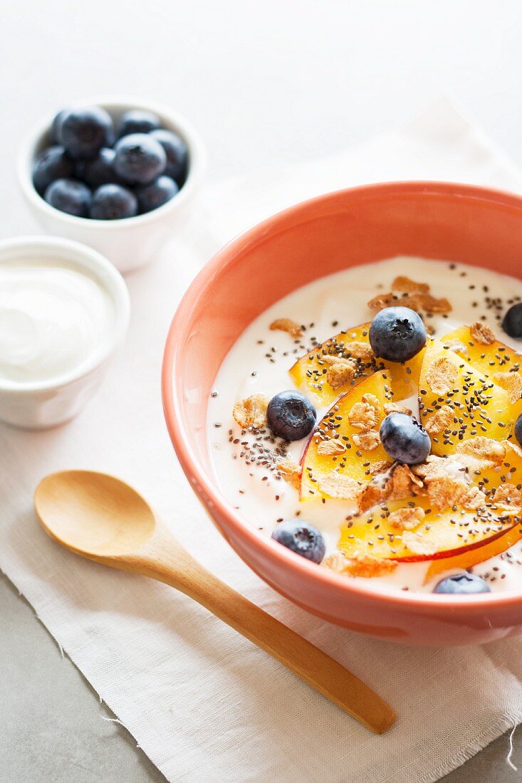 Yoghurt with peaches, blueberries, whole-grain flakes and chia seeds in a muesli bowl