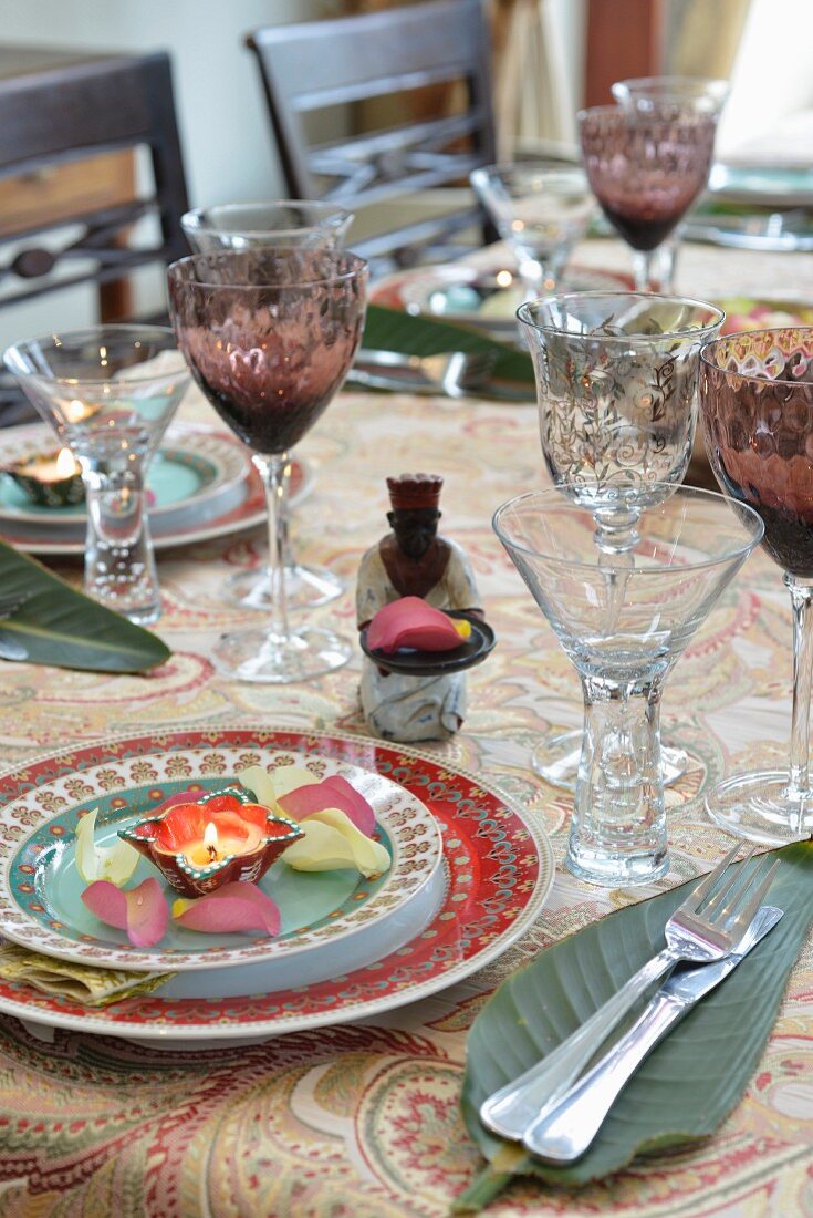 An exotically laid table with crystal glasses, banana leaves, tea lights and petals