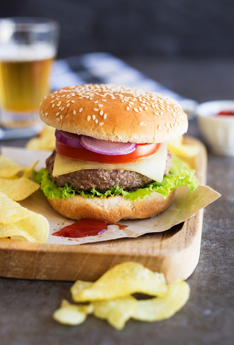 A hamburger with tomato, lettuce, onions and cheese, served with crisps and beer