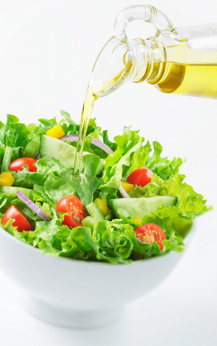 Öl auf Blattsalat mit Kirschtomaten, Gurken, Paprika und Zwiebeln gießen