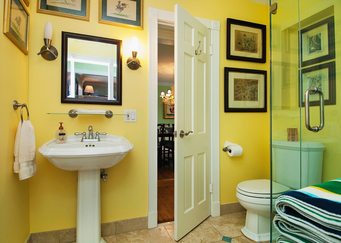 Washbasin, toilet and paintings mounted on yellow wall in bathroom; West Palm Beach; USA