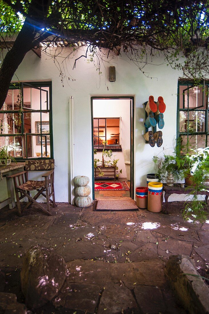 Summery terrace with weathered stone floor, boots hung on wall and view into illuminated foyer