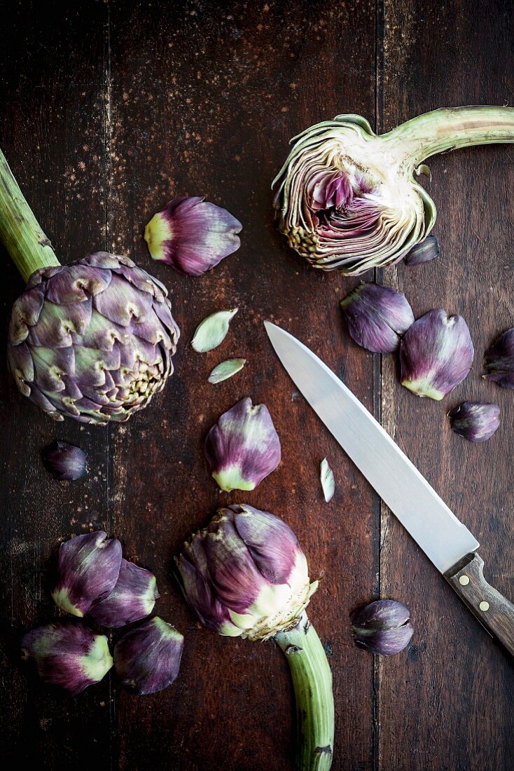 Artichokes, a knife and individual artichoke leaves on a wooden surface