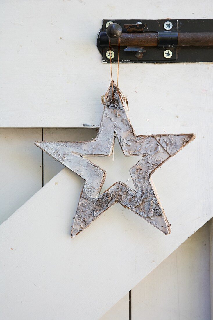 A star made from white-painted tree bark hanging from a bolt on a wooden gate