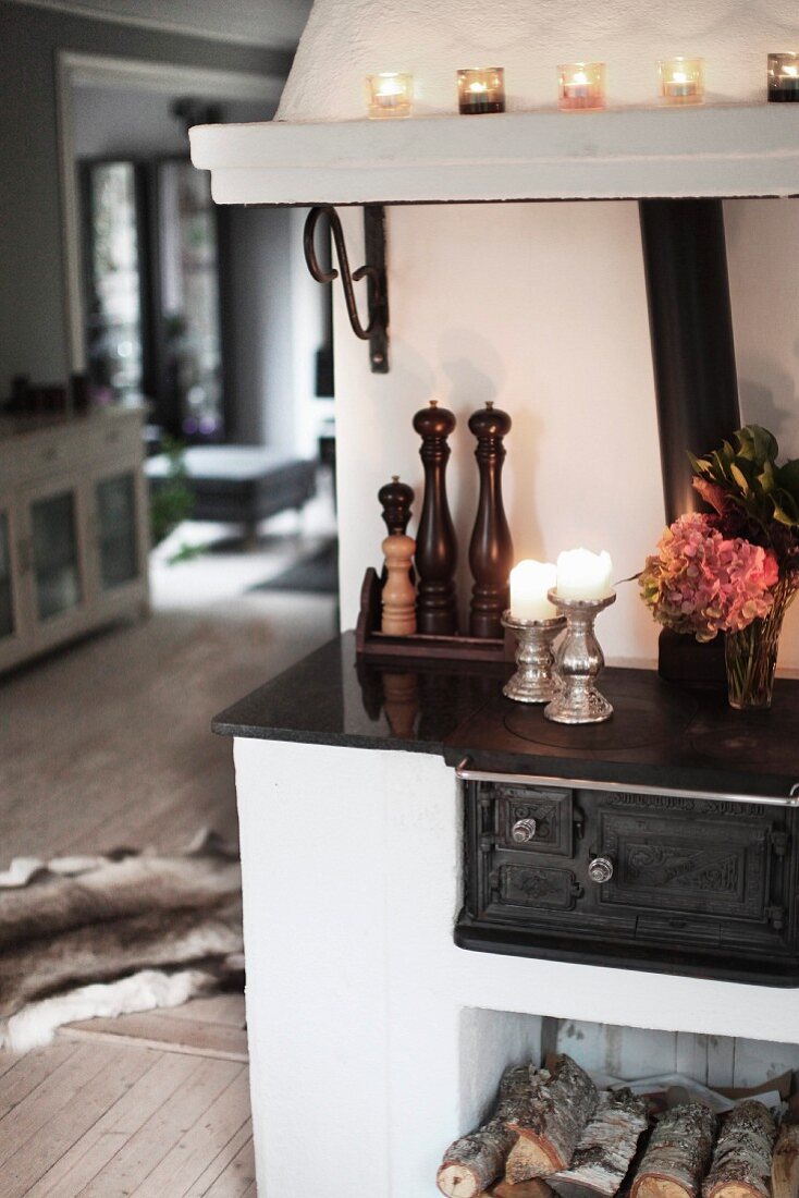 Lit candles on hob of wood-burning oven with firewood and chimney in open-plan living area of country house