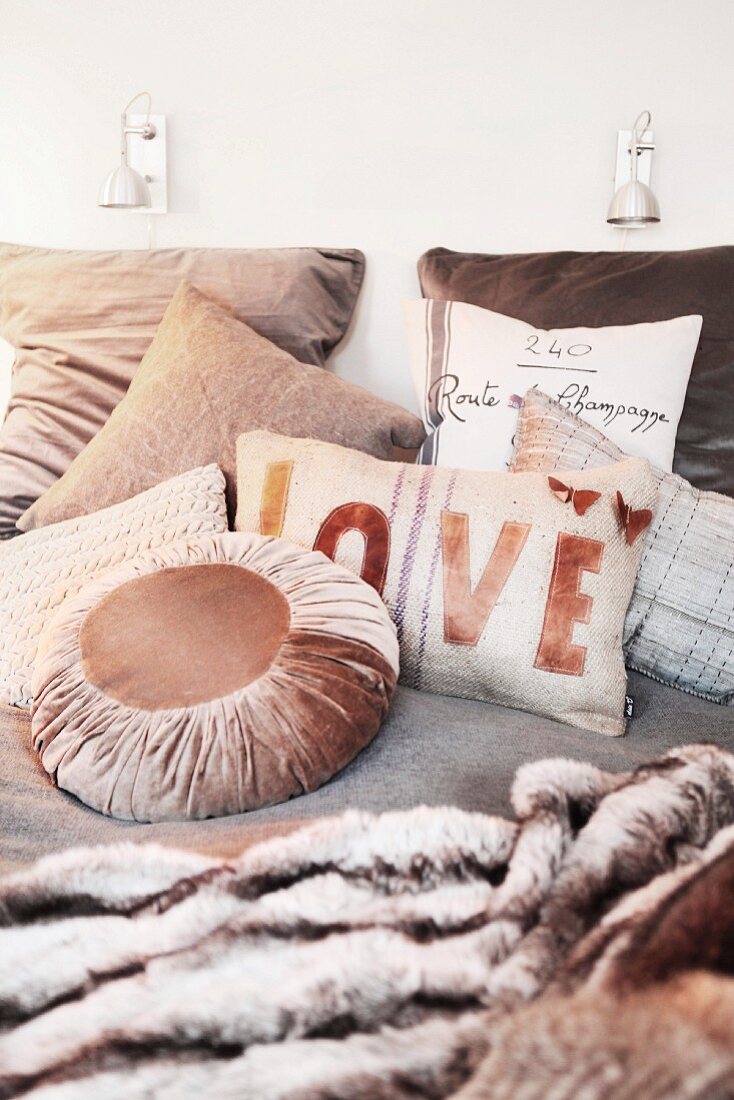 Cosy double bed with collection of beige scatter cushions and soft fur blankets