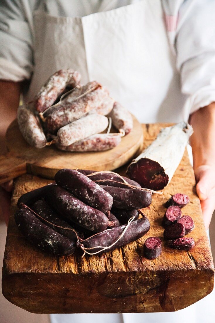 A butcher holding a selection of sausages on a wooden board