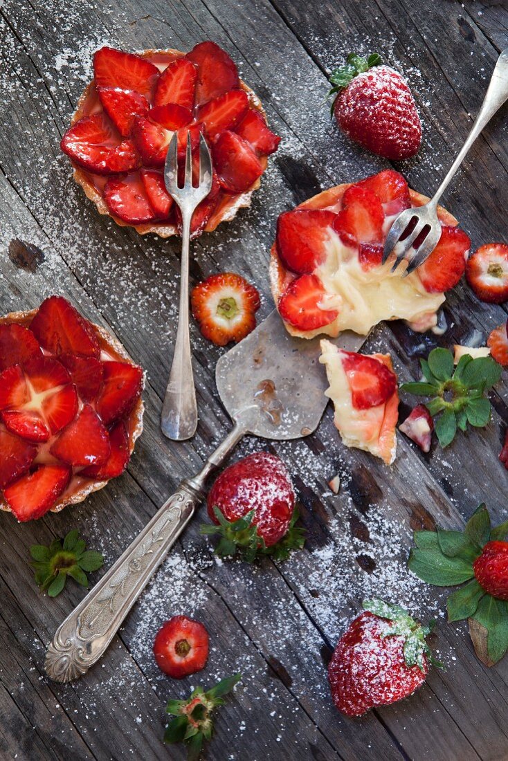 Erdbeertörtchen mit Vanillecreme und Puderzucker auf Holztisch