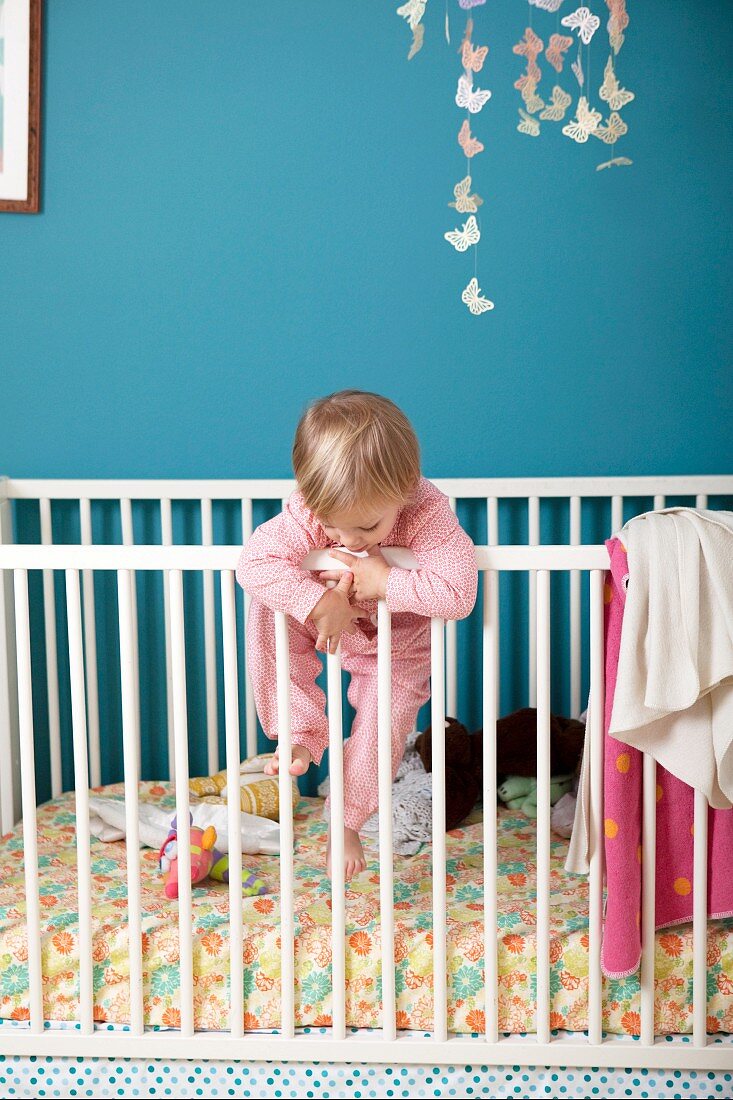Kleines Mädchen klettert an den Gitterstäben vom Kinderbett hoch