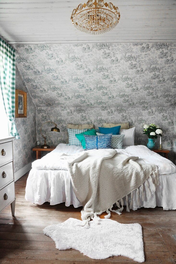 Gemütliches Landhaus Schlafzimmer mit tapezierter Dachschräge, Dielenboden und weiß bezogenem romantischem Doppelbett