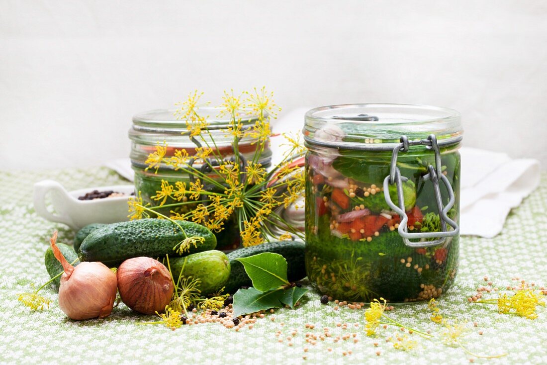 Two jars of homemade gherkins surrounded by ingredients
