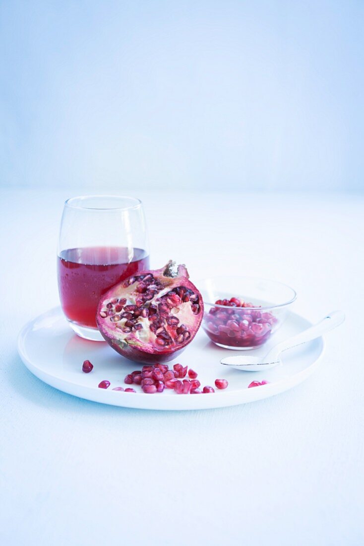 A glass of pomegranate juice, half a pomegranate and pomegranate seeds