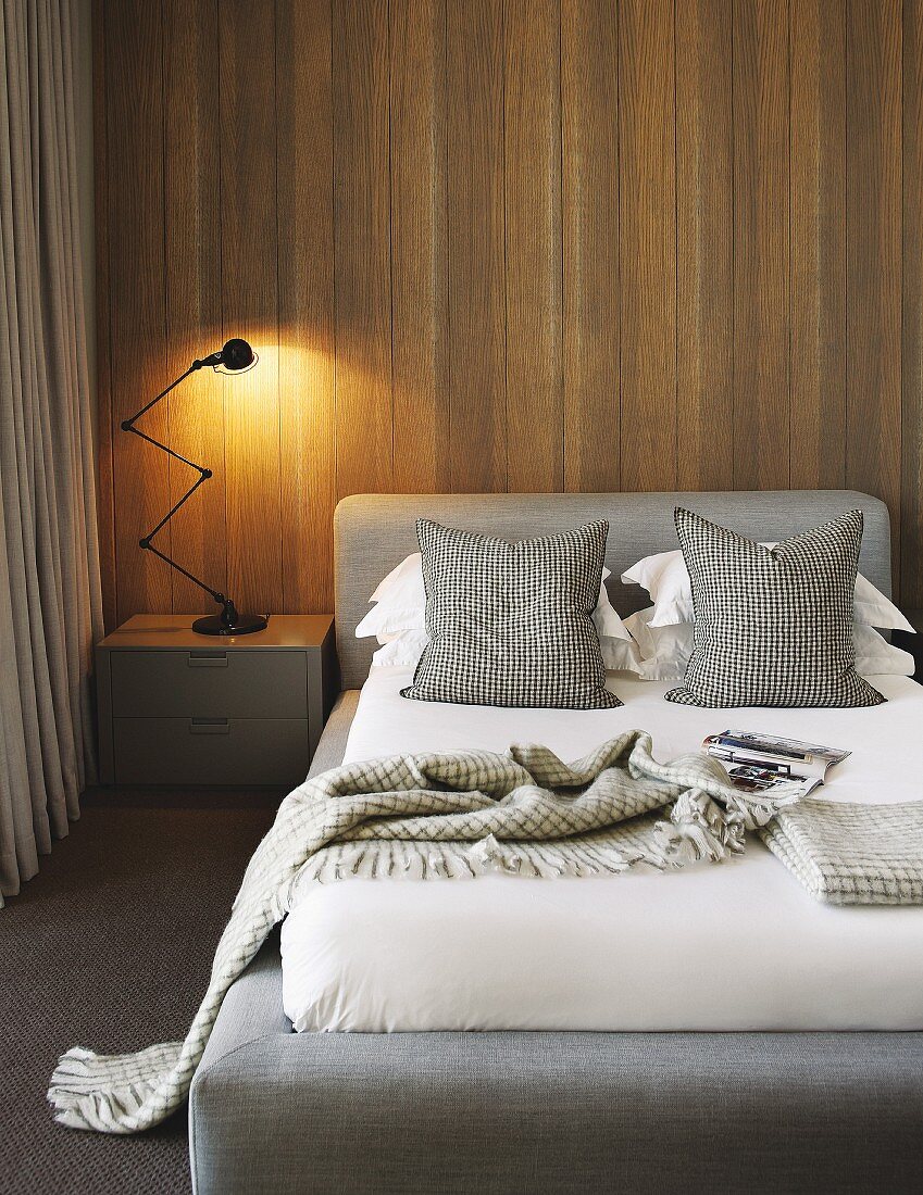 Classic table lamp on bedside cabinet next to bed with upholstered headboard against wood-clad wall