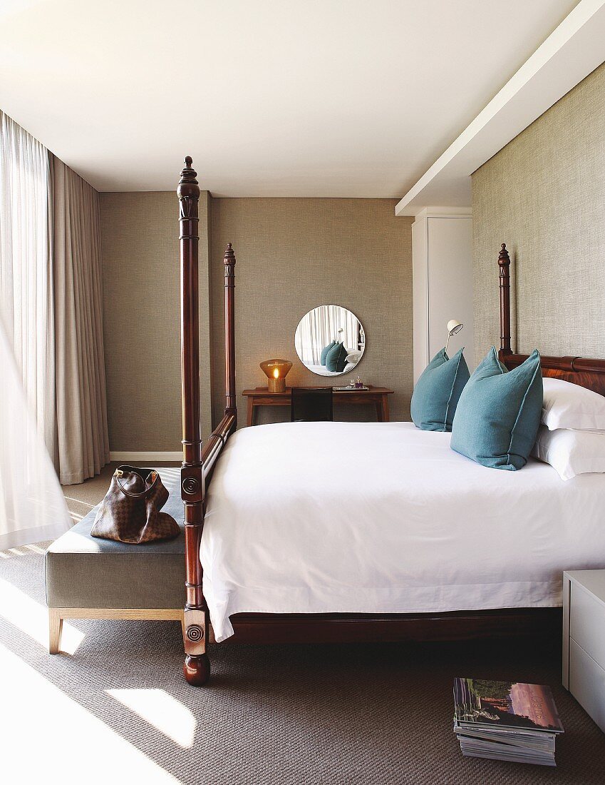 Elegantes Doppelbett mit Holzsäulen, an Bettende gepolsterte Sitzbank in klassischem Schlafzimmer