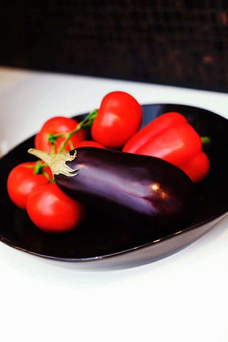 Tomaten, rote Paprika und Aubergine in schwarzer Schale