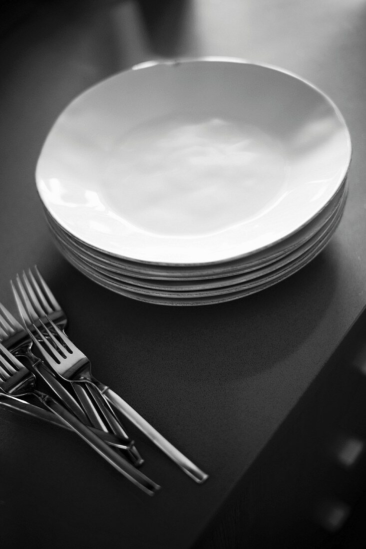 Gestapelte weiße Teller und mehrere Gabeln auf grauem Tisch