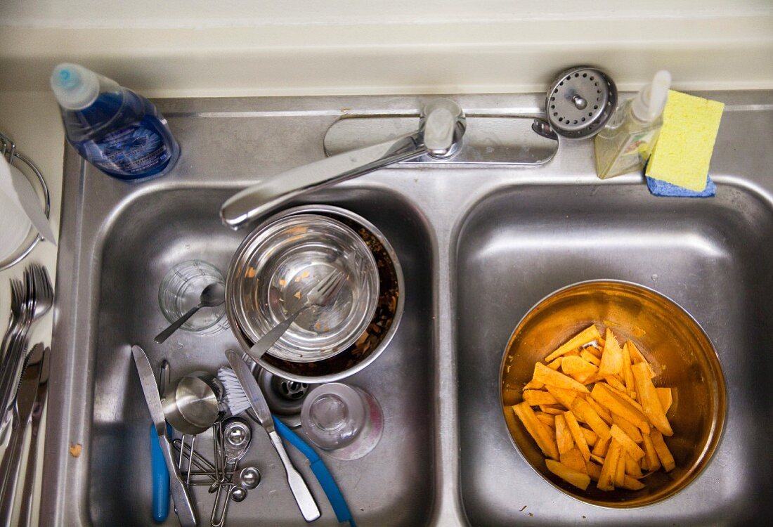 Sliced sweet potatoes and dirty dishes in a double sink