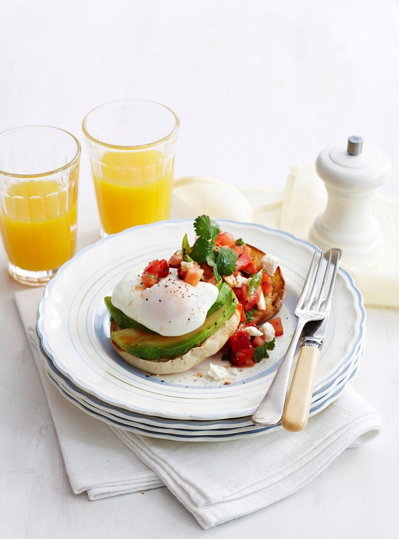 A bread roll topped with a poached egg, avocado and salsa served with orange juice (Mexico)