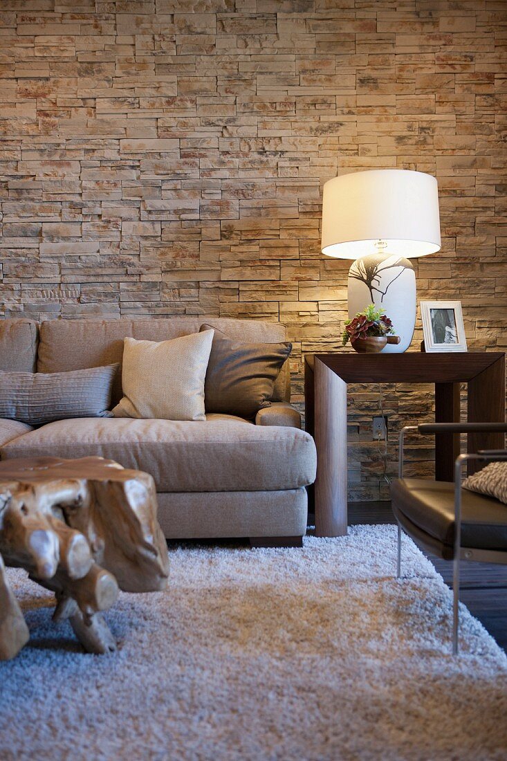 Wohnzimmer in Naturtönen mit Steinwänden, Sofa, Hochflorteppich & Couchtisch aus Baumwurzeln