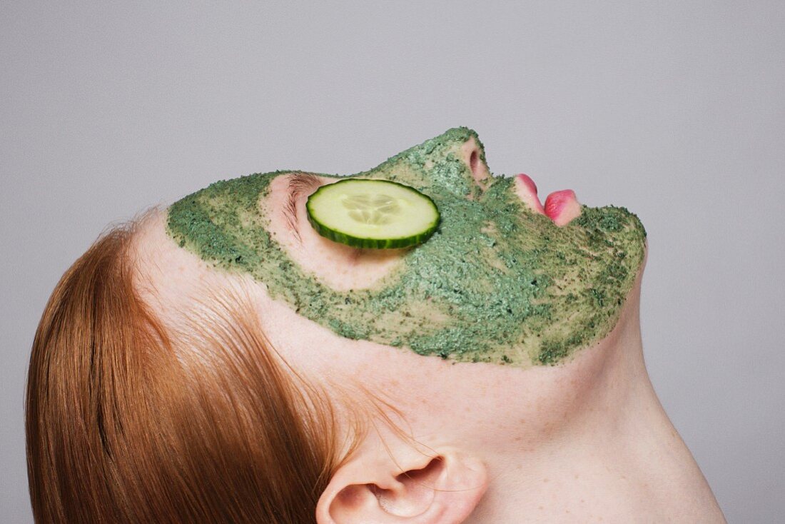 Junge Frau mit grüner Gesichtsmaske und Gurkenscheiben auf den Augen