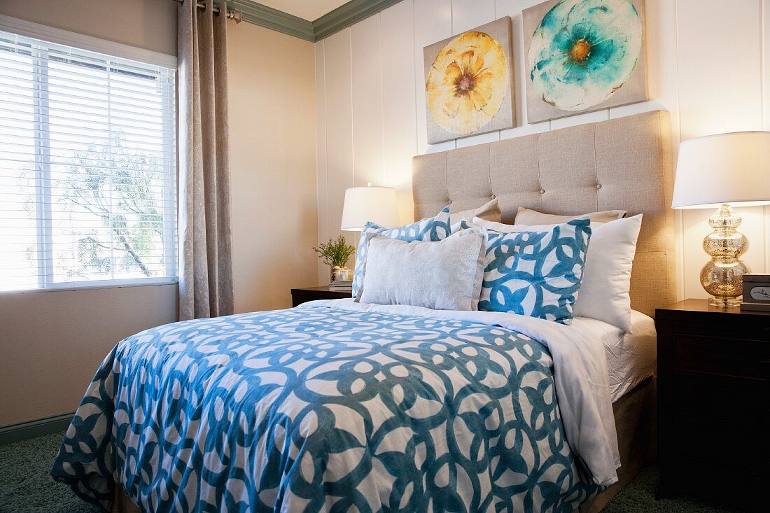 Lit table lamps by bed with picture frames on wall in bedroom