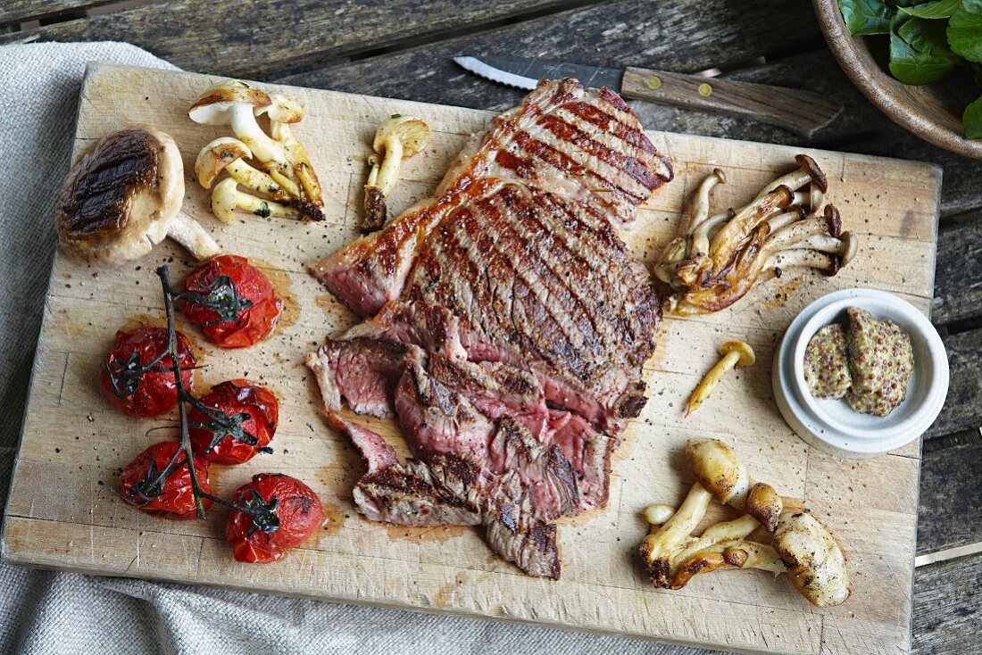 Grilled steak, mushrooms and tomatoes on a chopping board